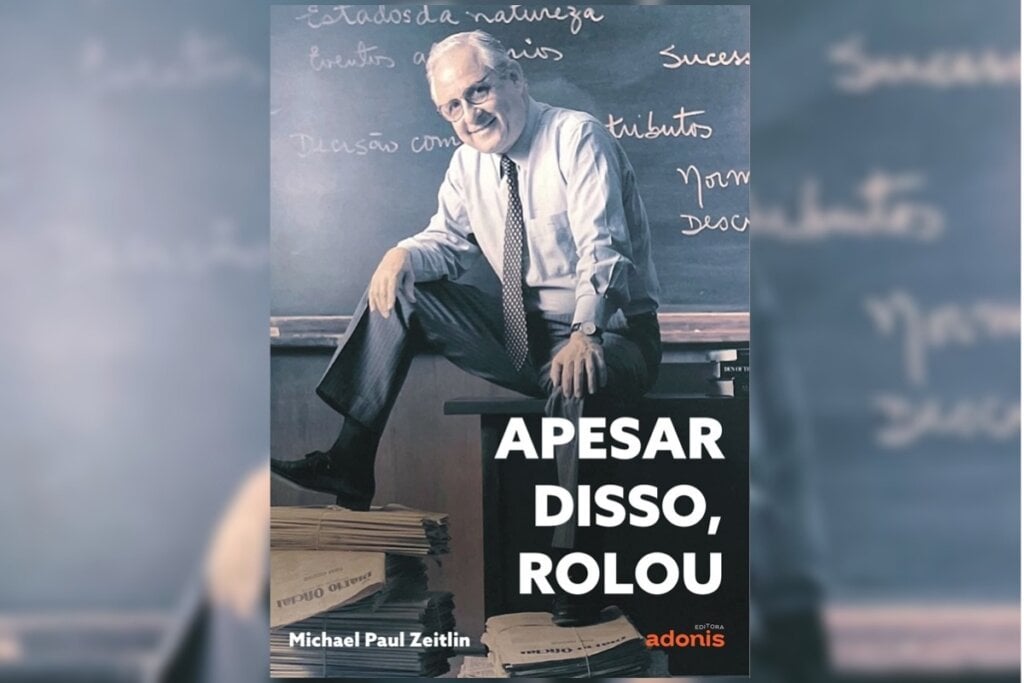 Foto de um homem sentado em uma mesa em frete a uma lousa na capa do livro 'Apesar disso, rolou'