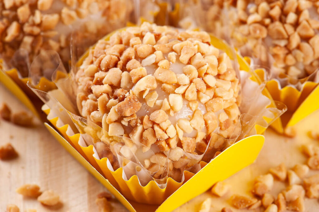 Brigadeiro decorado com pedaços de amendoim em cima de um papel amarelo