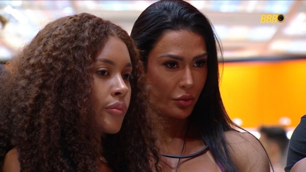 Giovanna Jacobina e Gracyanne Barbosa observam com atenção o desenrolar de uma dinâmica no reality show.