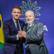 Lula e Macron de mãos dadas. Ao fundo, a bandeira do Brasil