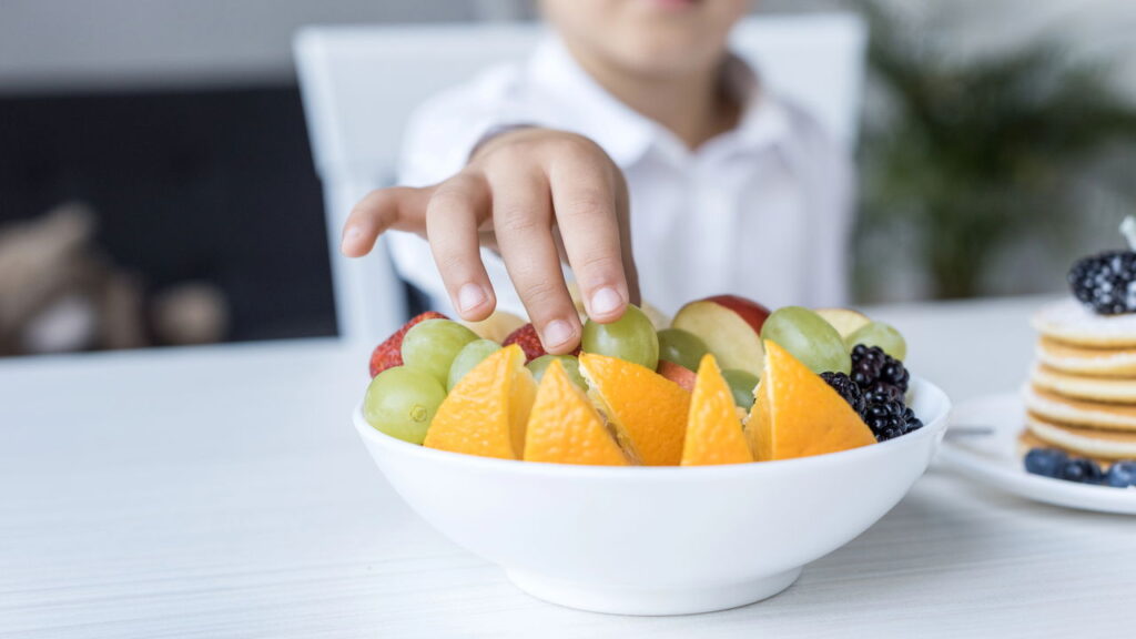 Criança comendo frutas (Créditos: depositphotos.com / AllaSerebrina)