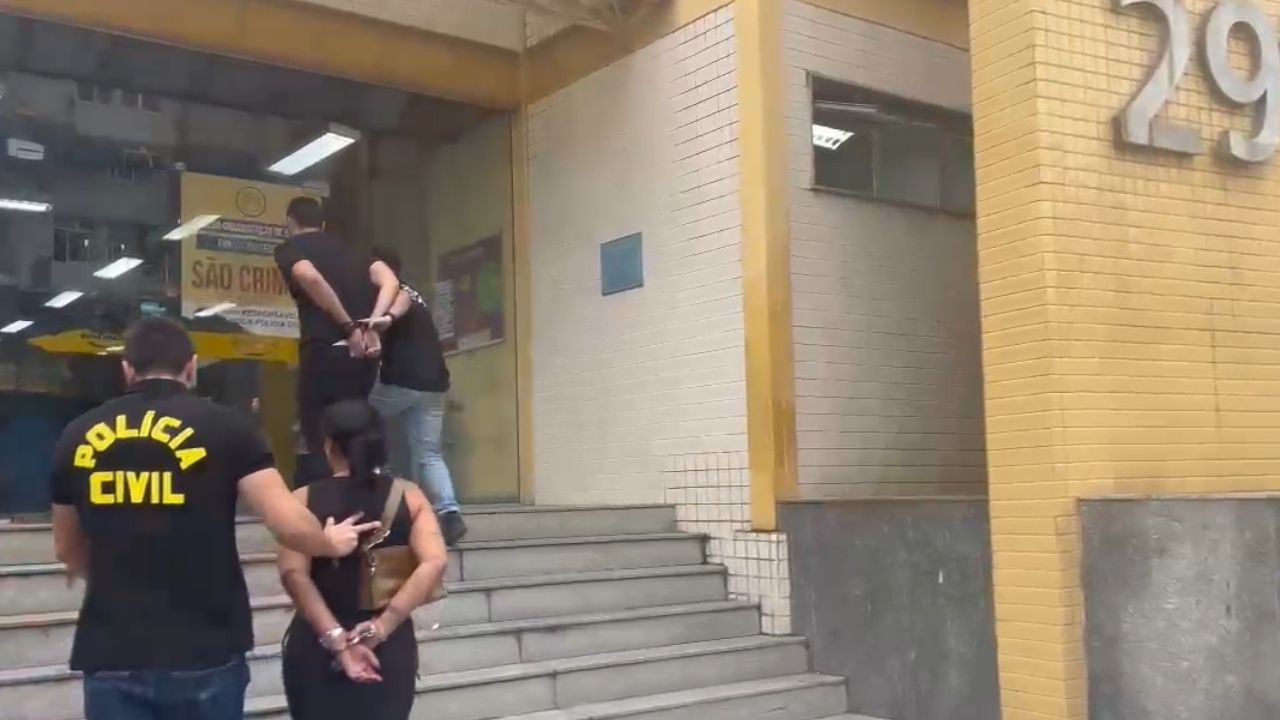 Reprodução de vídeo mostra casal de costas sendo escoltado por policiais civis entrando na delegacia de Madureira