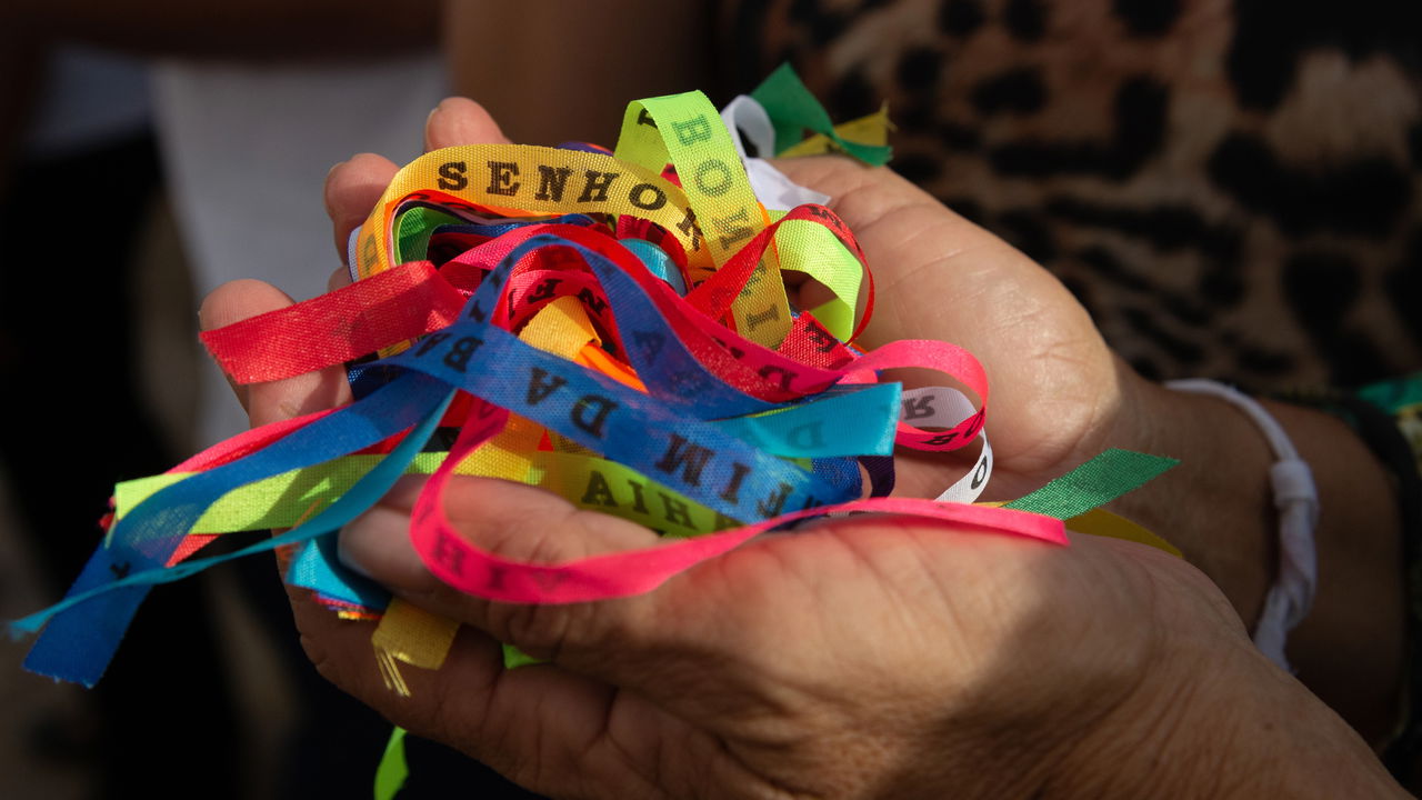 Mãos segurando fitas coloridas do Senhor do Bonfim, símbolo tradicional da fé e devoção associados à festa religiosa na Bahia