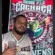 Torcedor do Fluminense morto à facadas aparece em foto segurando um copo e em frente a um banner da torcida.