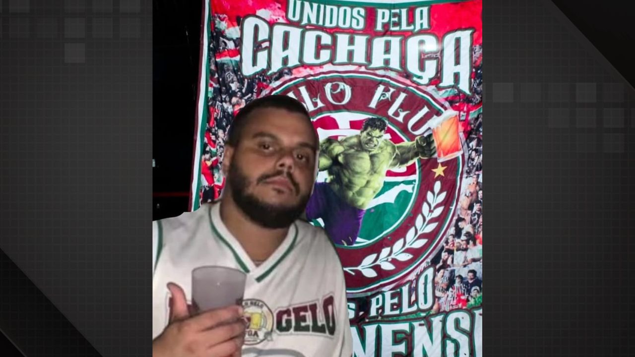 Torcedor do Fluminense morto à facadas aparece em foto segurando um copo e em frente a um banner da torcida.