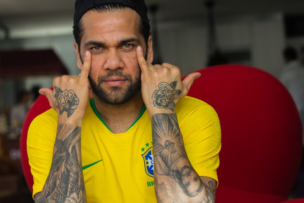 Daniel Alves com a camisa da seleção brasileira mostra tatuagens nos 2 braços e atingindo os olhos