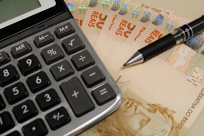 Imagem de uma calculadora, dinheiro e caneta