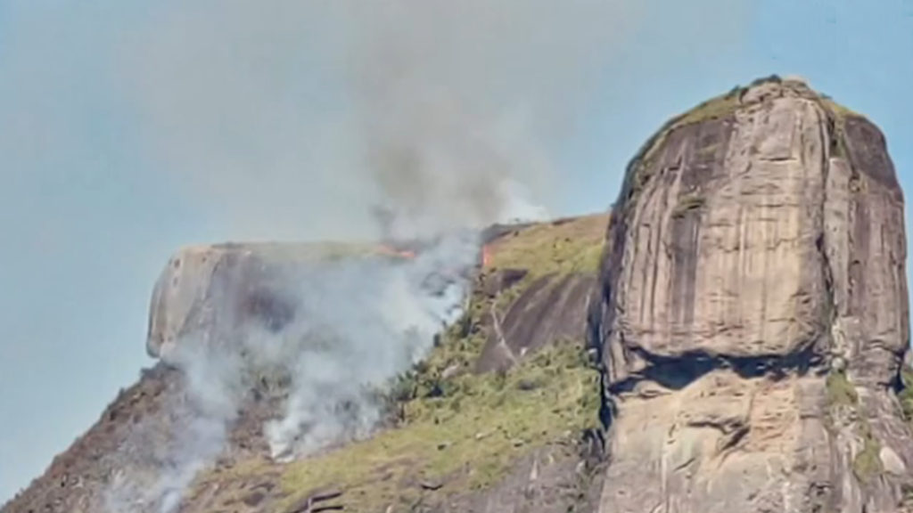 pedra da gávea pegando fogo e fumaça tomando conta do céu azul